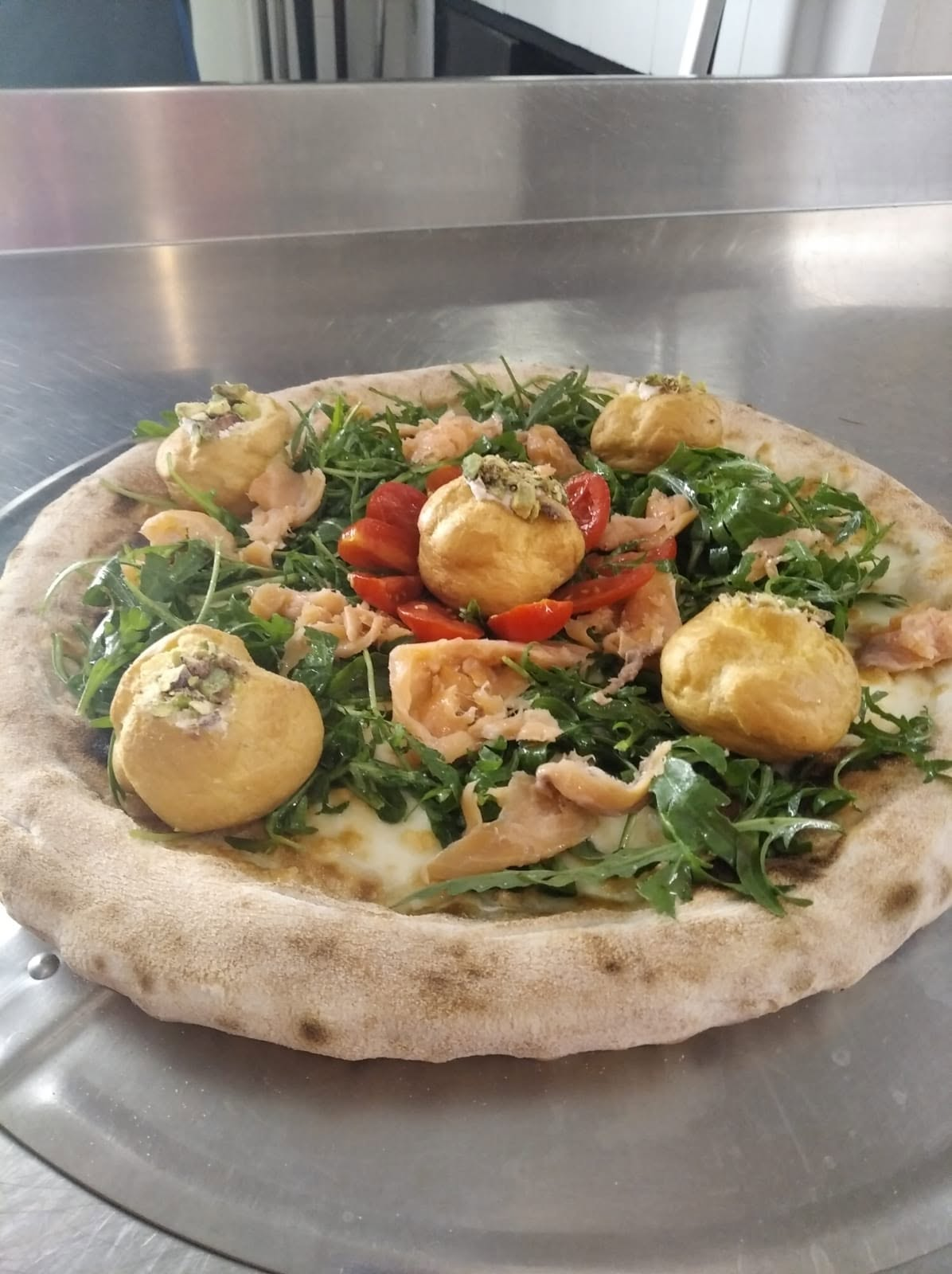 Pizza gourmet esclusiva con salmone affumicato, rucola, pomodorini e bignè salati farciti al pistacchio