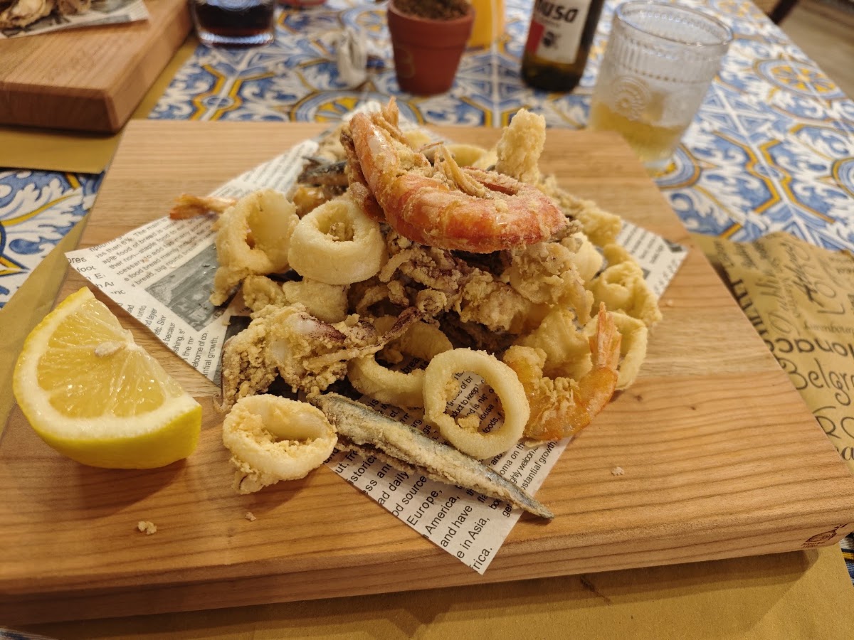Frittura mista di pesce servita su tagliere di legno nella sala interna della trattoria